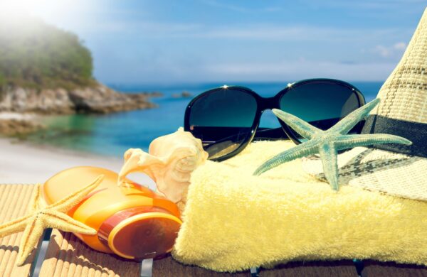 Opalovací krém, sluneční brýle, žlutý ručník na pláži u moře